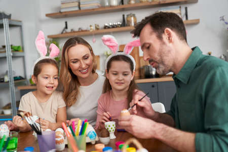 Happy caucasian family of four people decorates easter eggs at homeの写真素材