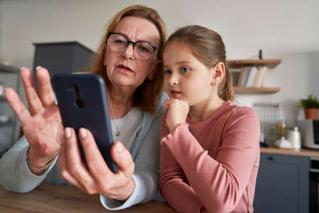 Close up of grandmother and her granddaughter using smart phone togetherの写真素材