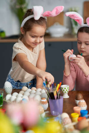 Vertical image of caucasian girls decorating easter eggs in the domestic kitchenの写真素材