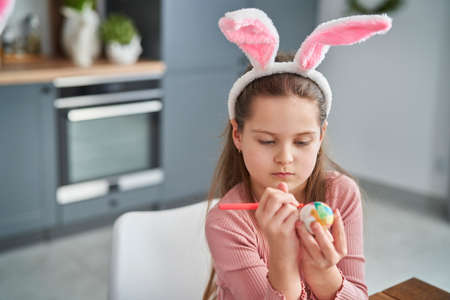 Focused caucasian girl decorating easter eggs in the domestic kitchen