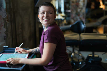 Caucasian tattoo artist designing motifs on digital tablet