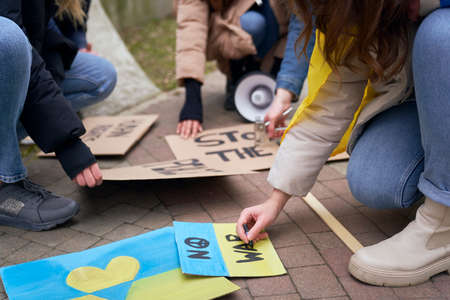 Group of young caucasian people preparing cardboard banners for manifest against Ukrainian war