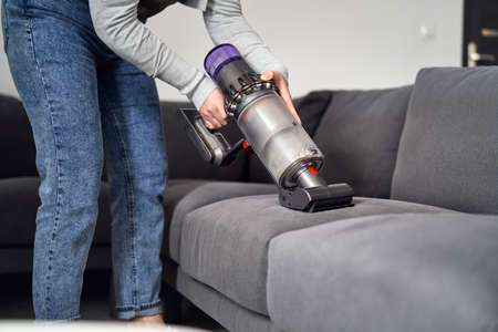 Close up of caucasian woman vacuuming sofa at homeの写真素材