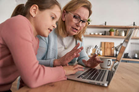 Caucasian of grandmother and her granddaughter looking on laptop at homeの写真素材
