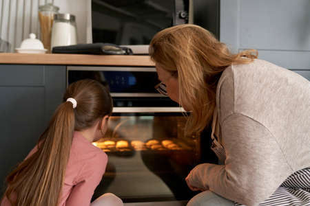 Caucasian grandmother and granddaughter checking the cookies in oven