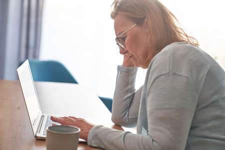 Focus senior woman using laptop at home
