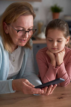 Caucasian grandmother and her granddaughter using smart phone together