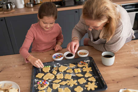 Caucasian girl with grandmother decorating cookies