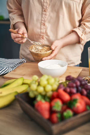 Woman adding muesli into the bowl with yogurtの写真素材