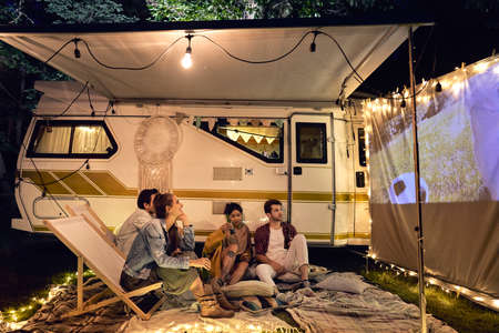 Young cheerful people watching a movie at camping siteの写真素材