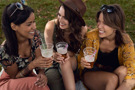Group of women sitting on the grass and drinking beer at summer festivalの写真素材