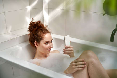 Caucasian redhead woman taking a bath and using mobile phone