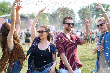 Group of caucasian young people dancing among confetti on music festival