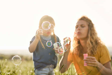 Caucasian mom with daughter blowing bubble at the meadowの写真素材
