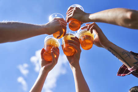Low angle view of hands toasting beer on blue sky at festivalの写真素材