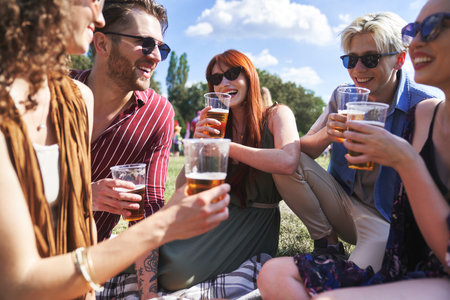 Group of young caucasian friends sitting on grass, drinking beer and having fun on music festivalの写真素材