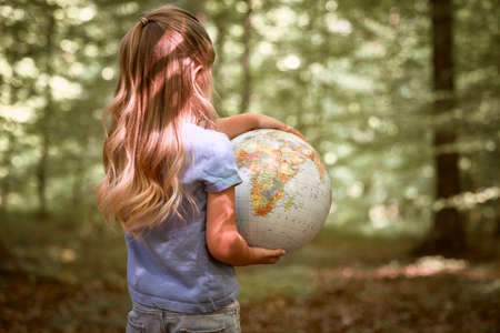 Rear view little girl holding globe in hands at the forestの写真素材