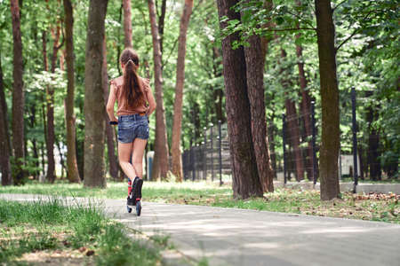 Rear view of girl leaning on push scooter at the parkの写真素材