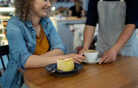 Unrecognizable waiter serving cup of coffee and piece of cake to the client at the tableの写真素材