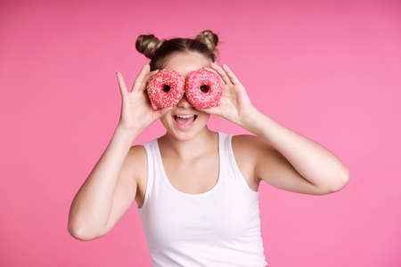 Caucasian teenage girl covering eyes with pink donutsの写真素材