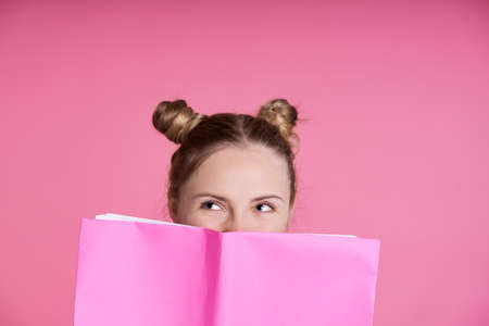 Close up of caucasian female teenager hidden behind pink paper notebook