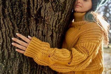 Caucasian woman holding arms around tree in park during the autumnの写真素材