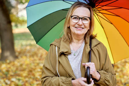 Portrait of senior woman under the umbrella at the park in autumn