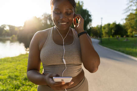 African American woman using mobile phone and earphones before exercising at the park in a summer dayの写真素材