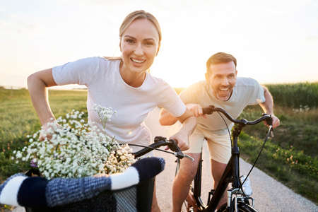 Playful caucasian couple having fun on a bike on village road and looking at camera