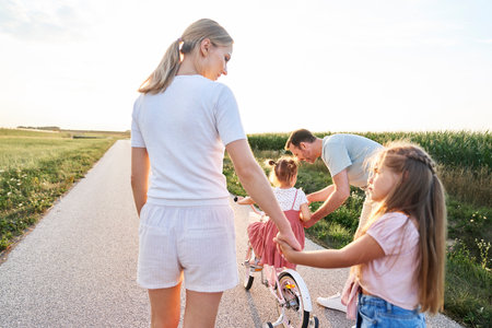Family of four caucasian people spending time on walking and riding a bike on village roadの写真素材