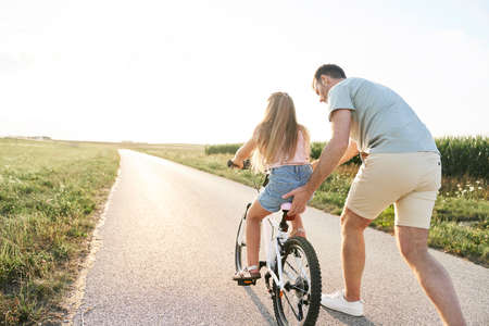 Father teaching his little daughter how to ride a bikeの写真素材