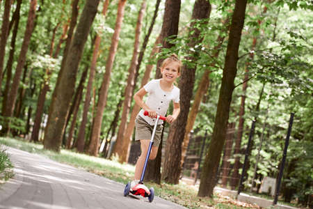 Smiling girl have fun on push scooter at the parkの写真素材