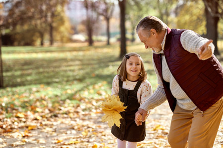 Little girl spending time with grandfather at the park in autumnの写真素材