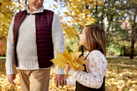Little girl spending time with grandfather at the park in autumnの写真素材