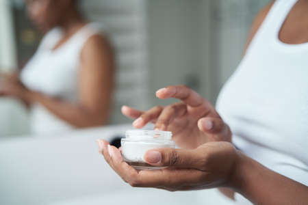 Young African-American woman about to apply face cream in the mirror reflection