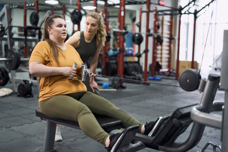 Caucasian plus size woman with her trainer working out in gym