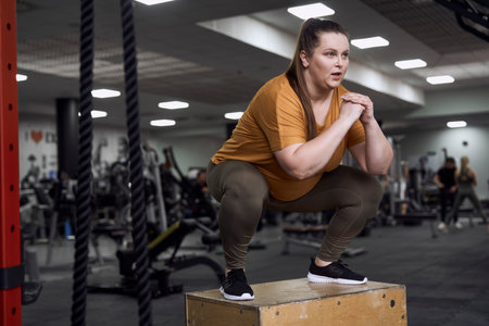 Woman with overweight jumping at the box in the gym