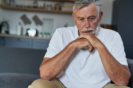 Senior caucasian man with mental problem sitting on couch in homeの写真素材