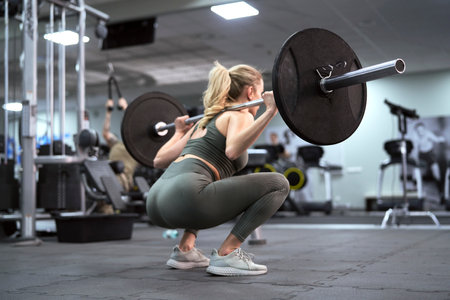 Rear view of blonde caucasian woman making squats with barbellsの写真素材