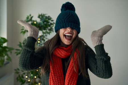 Funny caucasian woman wearing hat gloves and scarf at home during the Christmaの写真素材