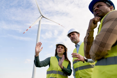 Low angle of team of caucasian and latin engineers standing on wind turbine field and discussingの写真素材
