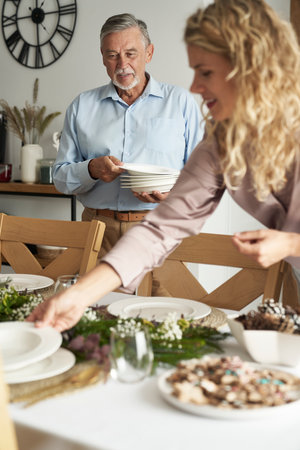 Cheerful caucasian senior man and young woman preparing the table for Christmas Eveの写真素材