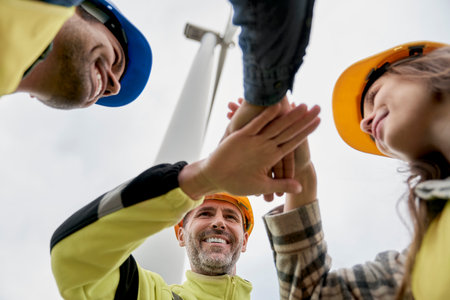 Low angle view of team of engineers bringing hands together after work on wind turbine fieldの写真素材