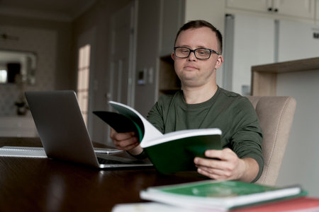 Man with down syndrome learning at home from paper bookの写真素材