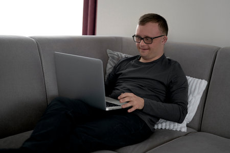 Man with down syndrome using laptop at home while sitting on sofa