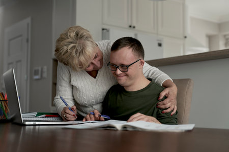 Mother hugging caucasian man with down syndrome while learning at homeの写真素材