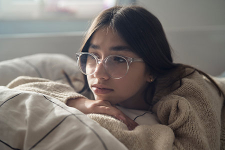 Close of pensive caucasian teenage girl lying on bed and looking away