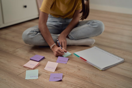 Unrecognizable caucasian teenage girl sitting on floor and making notes on flash cardsの写真素材