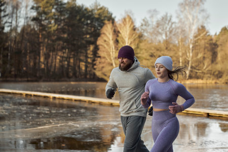 Adult caucasian couple running outdoors in the winter by the lakeの写真素材