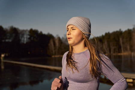 Side view of adult caucasian woman jogging on beach by the lake in the winter